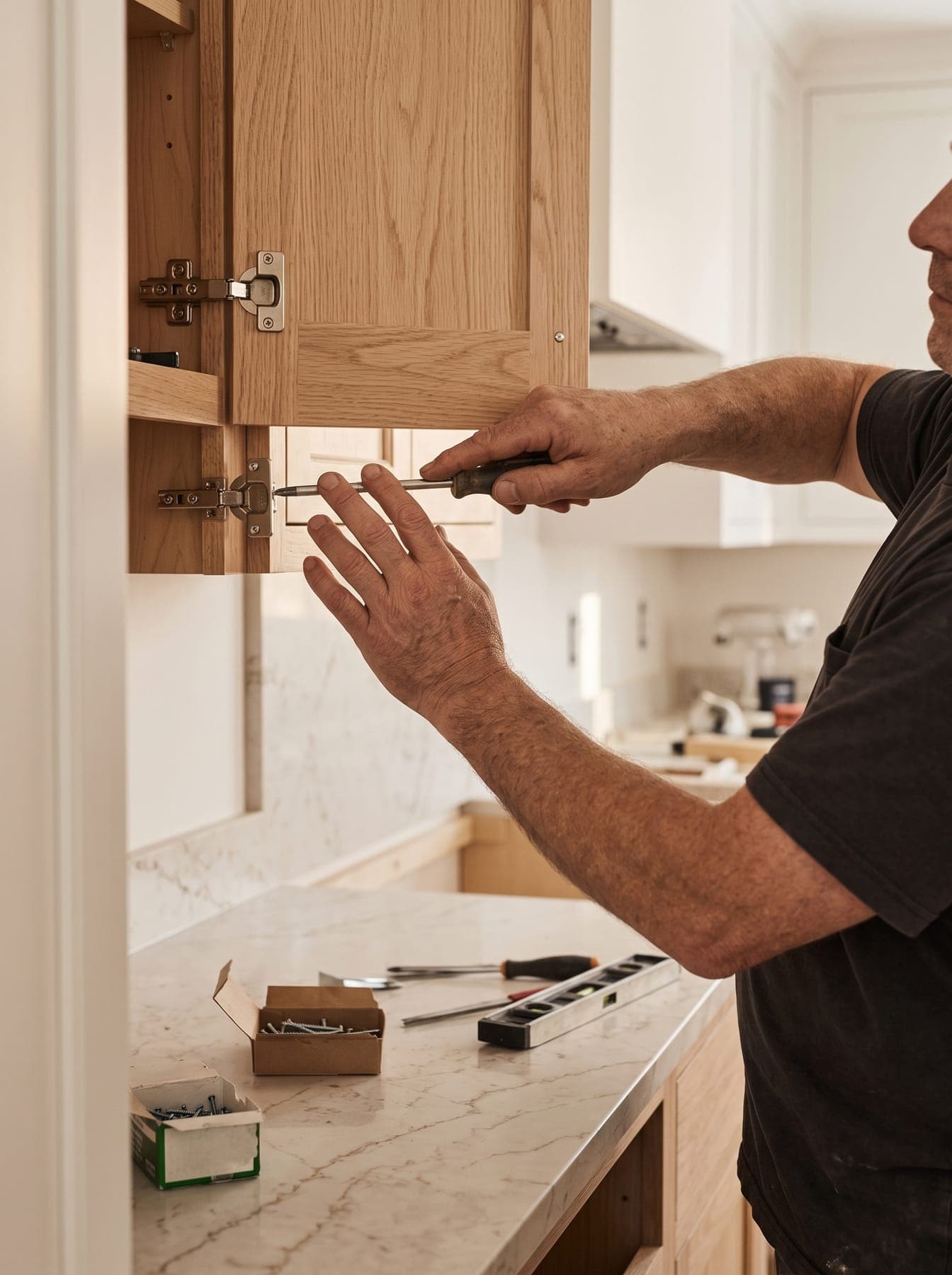 Menuisier qui règle la charnière d’une porte de meuble haut de cuisine en bois clair