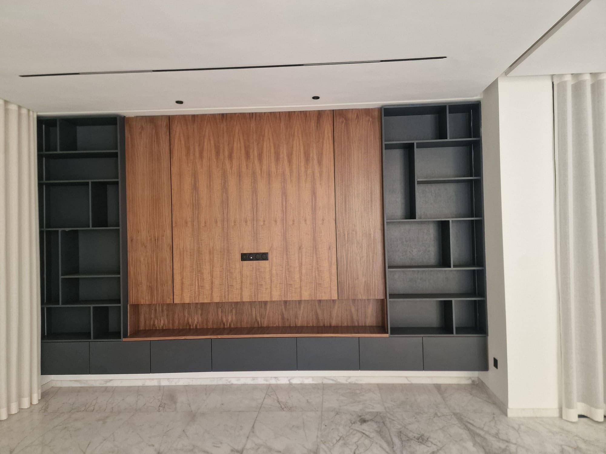 Séjour avec bibliothèque anthracite, panneau central en bois et rideaux