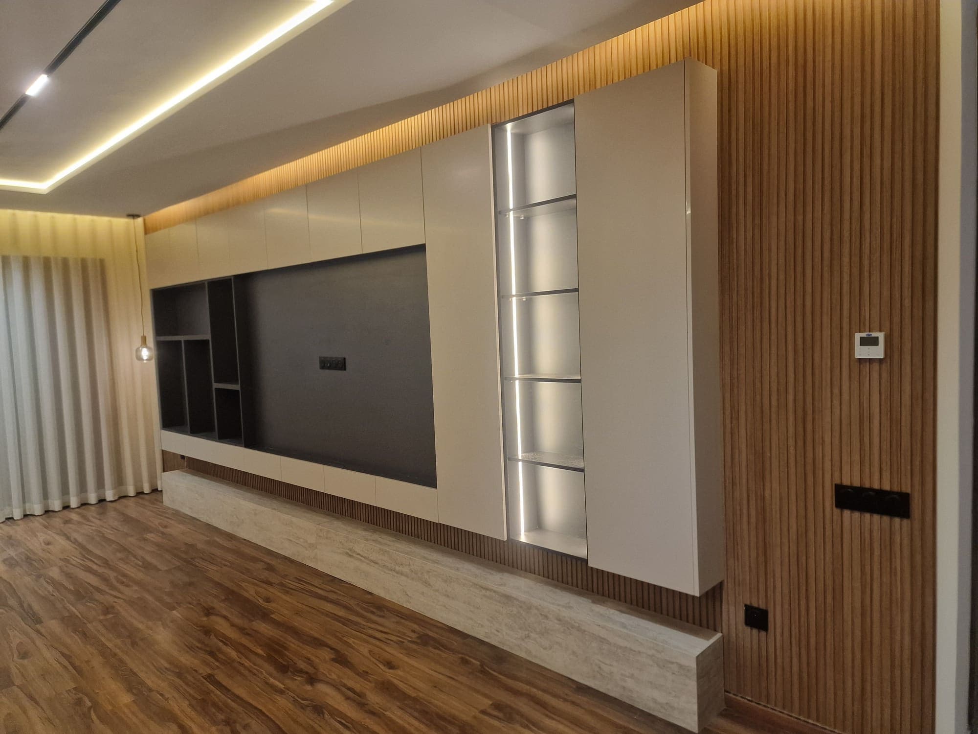 Mur TV avec habillage en lames de bois, meuble bas laqué et éclairage indirect