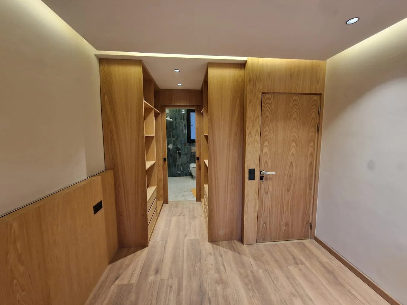 Couloir bordé de placards en bois clair, avec une porte en bois à poignée noire au fond et un lambris mural