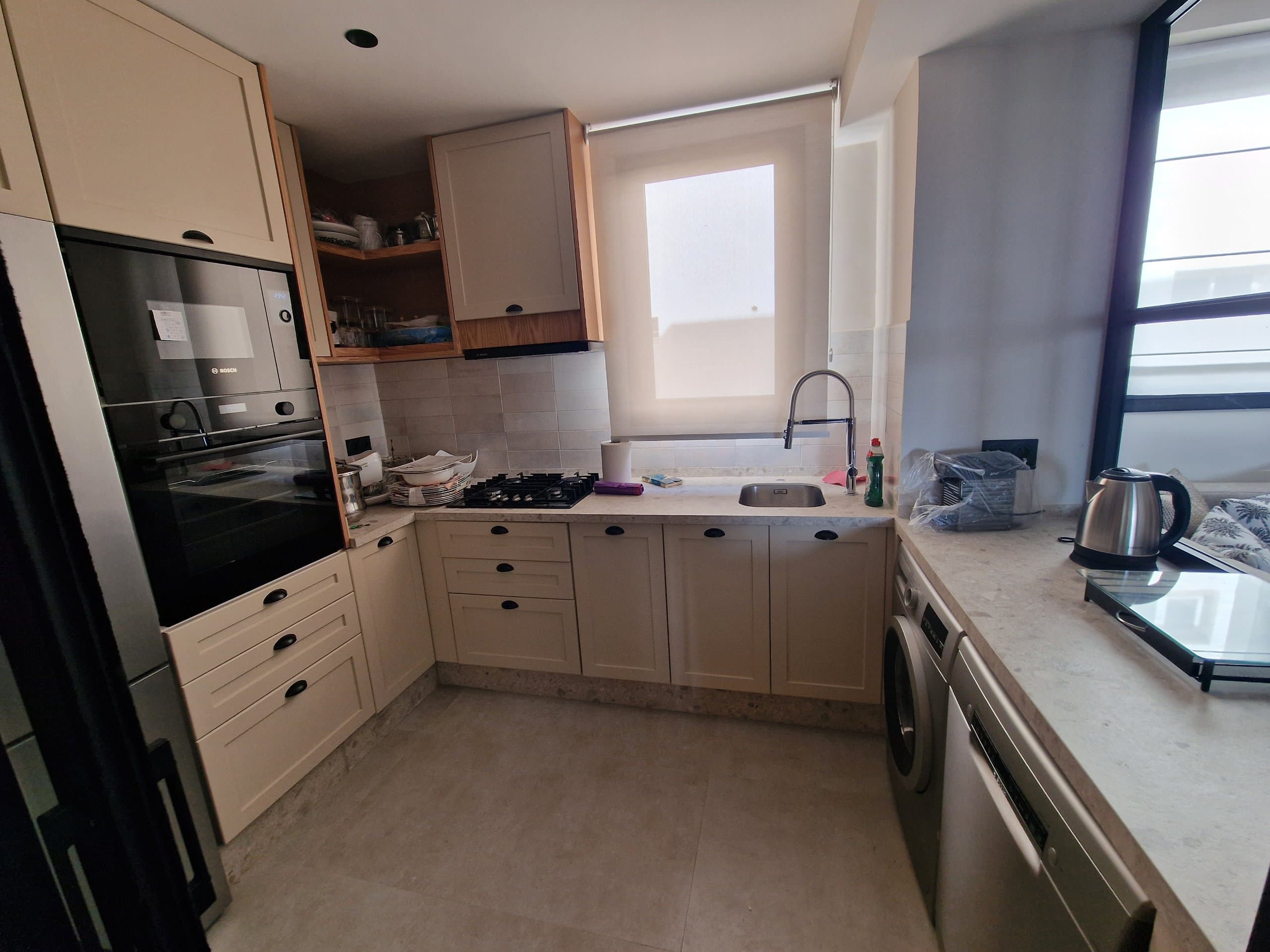 Cuisine laquée en L à Agadir : façades à cadre crème, poignées coquille noires, plaque de cuisson et hotte